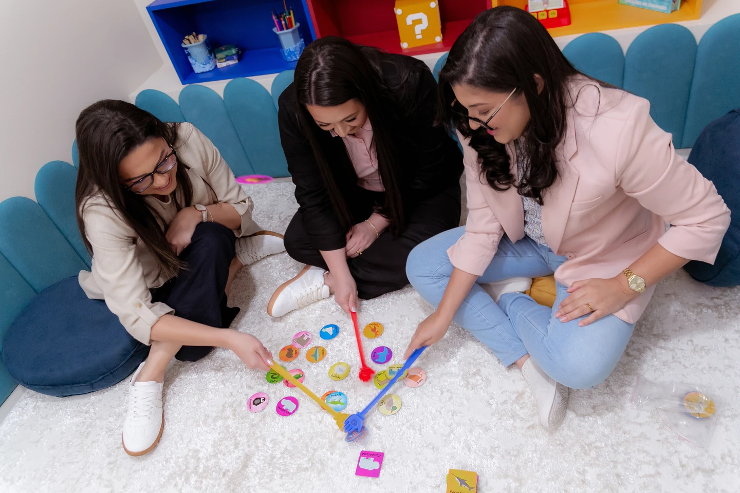 Três profissionais da Psycomind com um jogo de pesca e peças coloridas na sala infantil